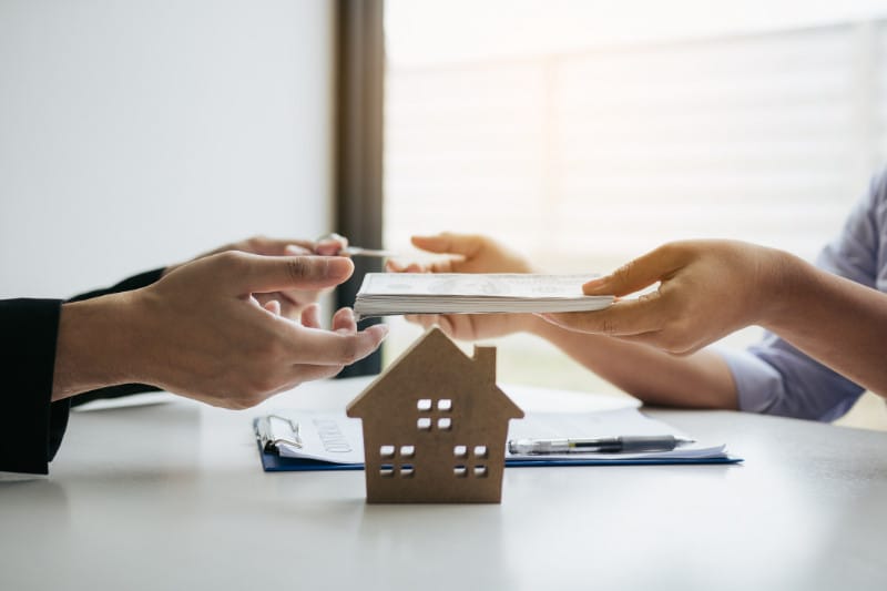 Two people review a tablet featuring a house model, illustrating the choice between hiring a real estate agent or purchasing alone.
