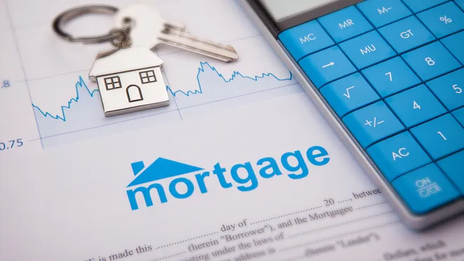 Keys and a house keychain on a mortgage document beside a blue calculator, symbolizing home financing.