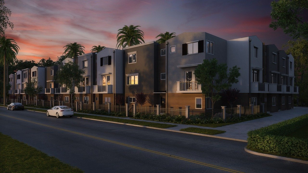 Modern apartment complex with palm trees, set against a sunset sky, showcasing balconies and a tranquil street view.